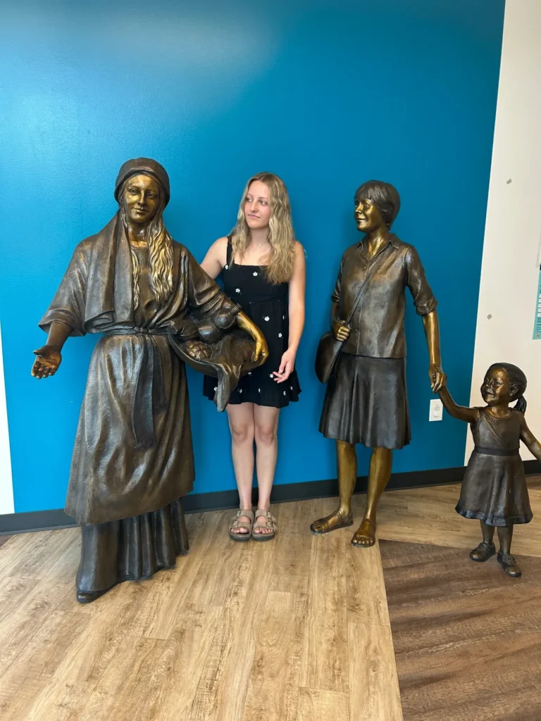 Tom White Studios, Inc | St Angela Merici & Dorothy Kazel Saint Angela Merici Statue & Dorothy Kazel bronze portrait sculpture scene commissioned by Urban Community School and created by Tom White, Sculptor. St Angela Merici was the founder of the Ursuline nuns in the 1400’s. Photo with Isabella, the artist's granddaughter who posed for the sculpture.
